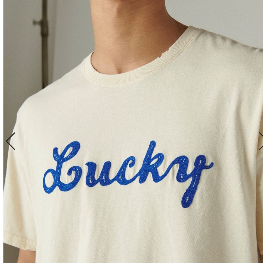 LUCKY T SHIRT WITH EMBROIDERED NAVY SCRIPT ON CREAM. DISTRESSE…